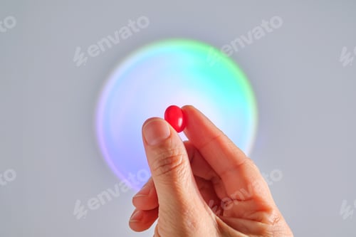 Preview: A red tablet of a vitamin complex in a hand.