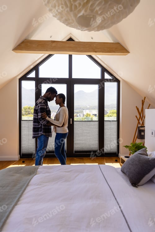 Preview: Thoughtful african american couple embracing by window in bedroom