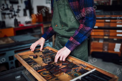 Preview: Crop of young craftsman looking through tray of wooden letterpress letters in print workshop