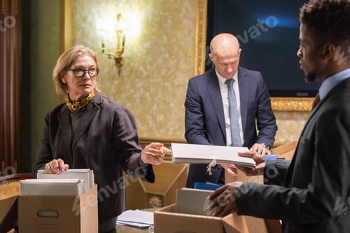 Preview: Mature blond female jurist passing folder with papers to young man