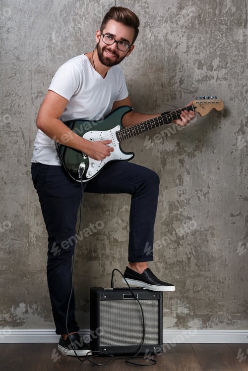 Preview: Stylish bearded guy with guitar against concrete wall