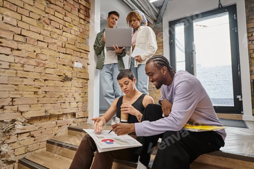 Preview: happy african man pointing at graphs, sitting with female colleague, discussing project, startup