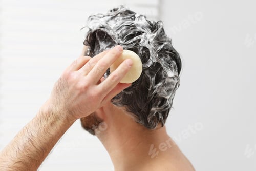 Preview: Man washing his hair with solid shampoo bar in shower, closeup