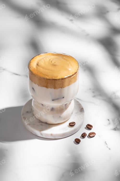Preview: Dalgona coffee. Whipped instant iced coffee in a glass with coffee beans and shadow