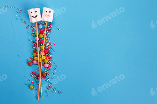 Preview: marshmallows on wooden skewers with color sweets on blue background