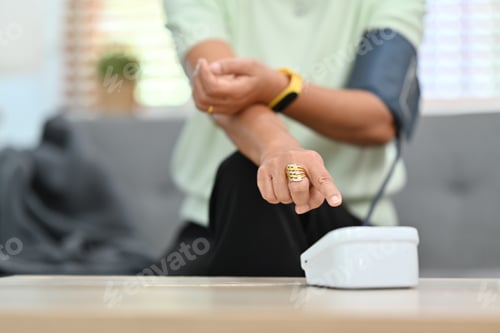 Preview: Cropped image of senior lady measuring blood pressure herself with tonometer at home.