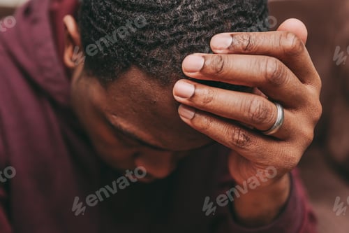 Preview: African American man with head in hand looking down and depressed