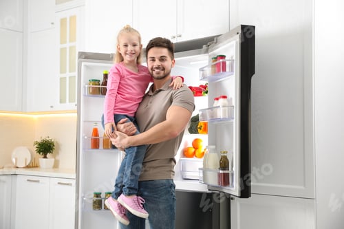 Preview: Young father with daughter near open refrigerator in kitchen