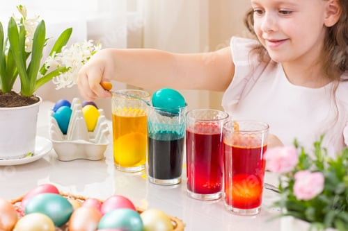 Preview: Cute little girl painting Easter eggs in glasses with liquid dye.