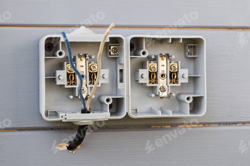 Preview: Double outdoor socket installation on gray wooden wall shows open casing and exposed wires