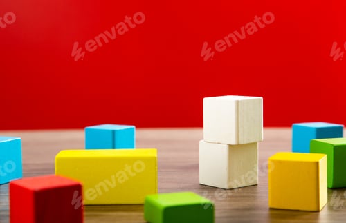 Preview: White wooden blocks towering over colorful cubes on table with red background