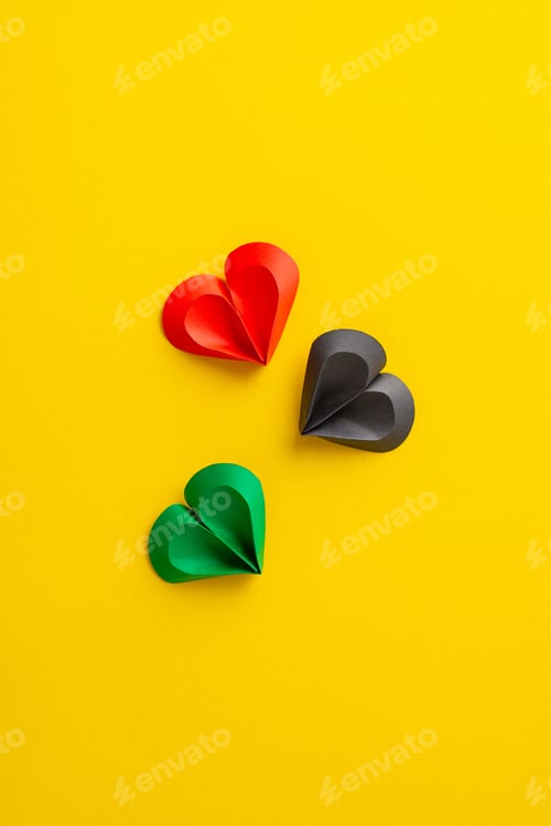 Preview: Three paper hearts in red, black, and green colors arranged on a vivid yellow vertical surface