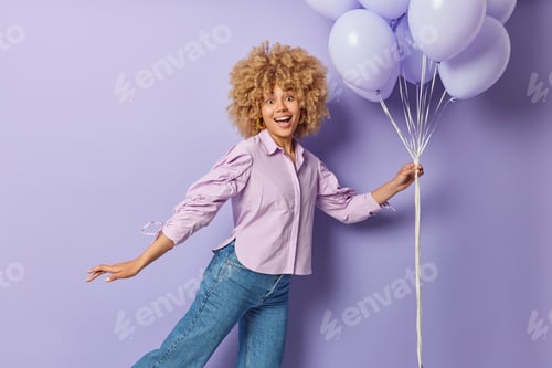Visualização: Foto ao ar livre de uma jovem alegre dançando despreocupada, chega à festa, segura um monte de balões de hélio, nós