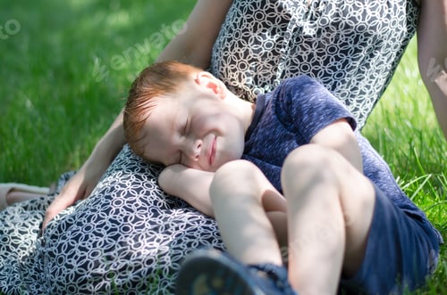 Preview: Children's sleep in nature. A little boy sleeps on his mother's feet in the park.