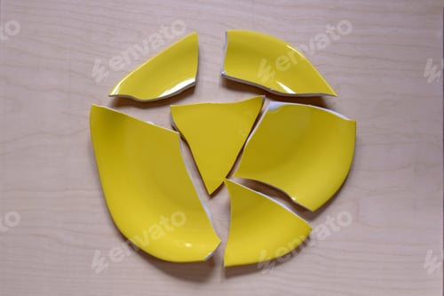 Preview: Fragments of broken yellow plate are located on light wooden surface