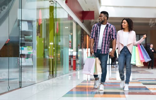 Preview: Seasonal Sales. Happy Black Couple Walking In Mall Center After Buying Clothes