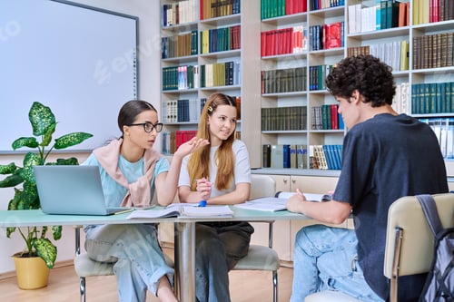 Preview: Group of students teenagers sitting together at desk in library preparing for tests exams