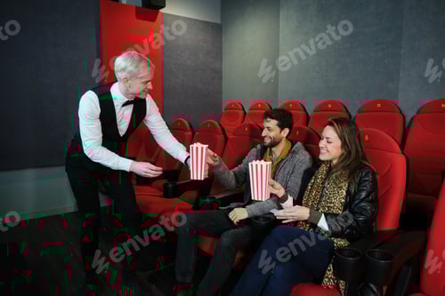 Preview: Waiter serving popcorn to couple in movie theater