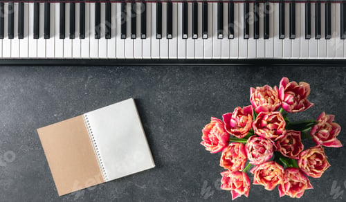 Preview: Piano, bouquet of tulip flowers and notepad on a dark background, top view.