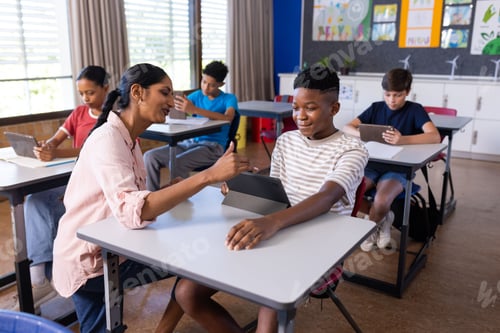 Visualização: Professora indiana ajudando estudante com tablet na sala de aula, outros estudantes estudando