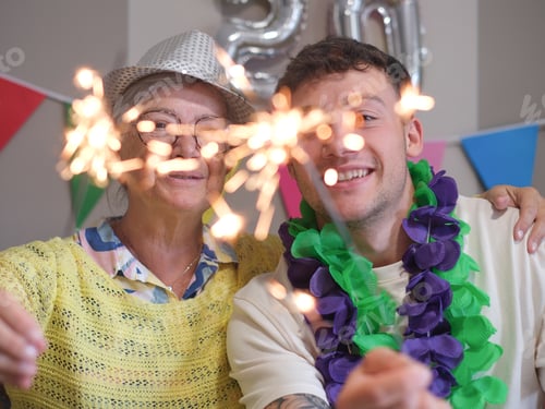 Preview: Joyful family birthday celebration at home, senior woman and young grandson holding sparkle lights
