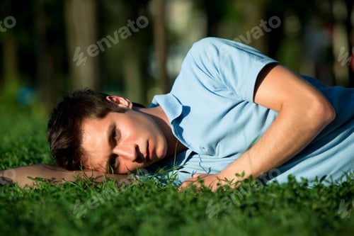Preview: Young man in casual clothing lying on green grass and looking at camera