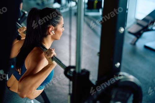 Preview: Female athlete using barbell while exercising strength during sports training in a gym.