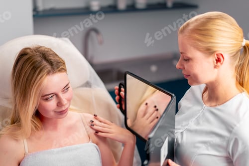 Preview: the beautician holds a mirror and shows the girl the result of a health cosmetic procedure for face