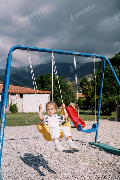 Preview: Little girl swings on a rope swing at the playground, looking to the side