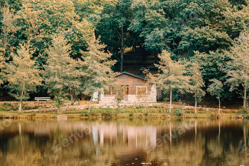 Preview: Cabin in front of a lake in the forest during autumn with copy space and colorful leaves and trees