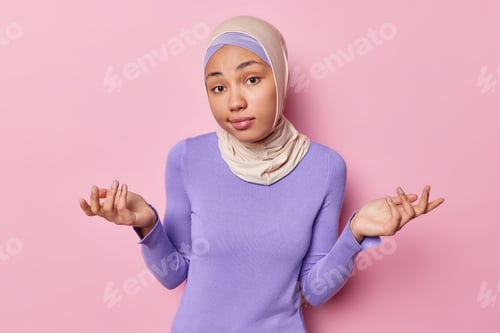 Preview: Clueless woman spreads palms feels hesitant or questioned being doubtful wears hijab and purple