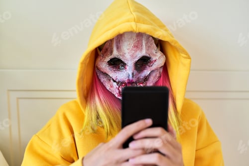 Preview: Halloween day, girl in scary face mask with hood makes video call on smartphone