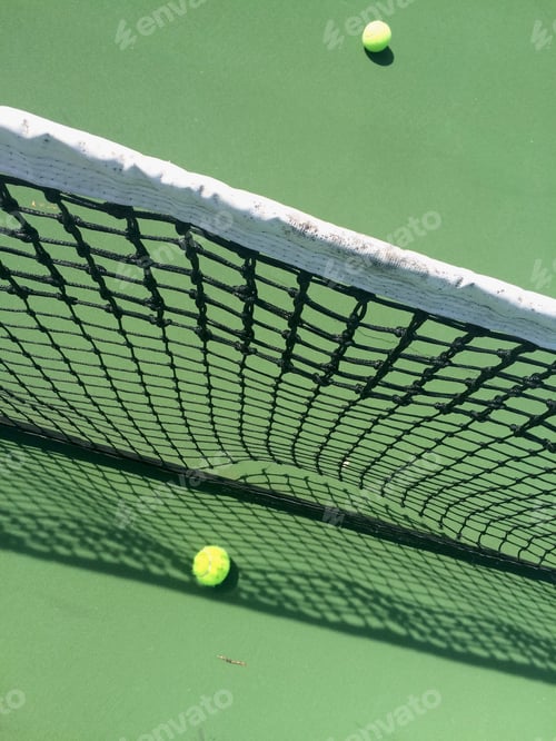Preview: Minimalistic view of a tennis net & tennis balls on the green tennis court with net’s shadows