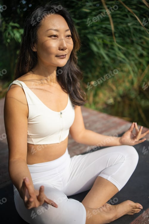 Preview: Young fit asian woman doing yoga by the lake in the morning park
