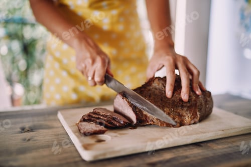 Preview: Housewife in an apron cuts juicy roast beef with a knife on a wooden cutting board