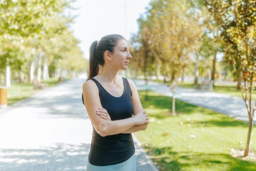 Preview: Athletic brunette woman resting after a fitness routine in the park on a sunny day.