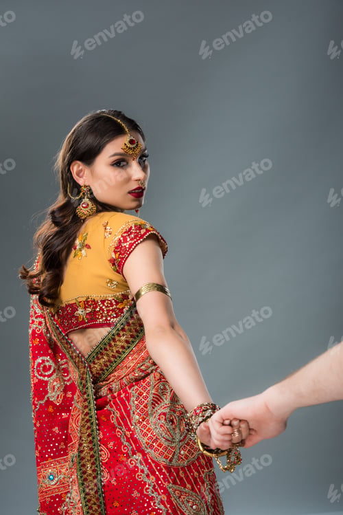 Preview: indian couple in traditional clothing holding hands isolated on grey
