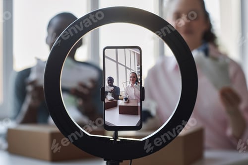 Preview: Screen of smartphone with intercultural bloggers unpacking ordered footwear
