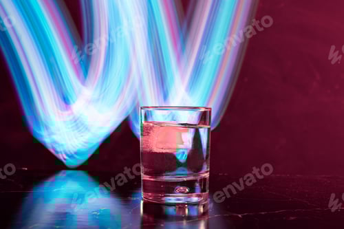 Preview: whiskey glass with ice on black backgound with neon light painings behind