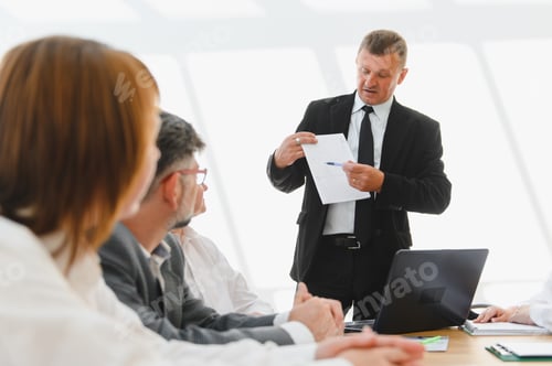 Visualização: Empresário sênior liderando uma reunião, explicando estatísticas aos colegas