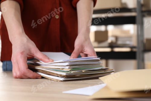 Preview: Woman with many different envelopes at table in post office, closeup