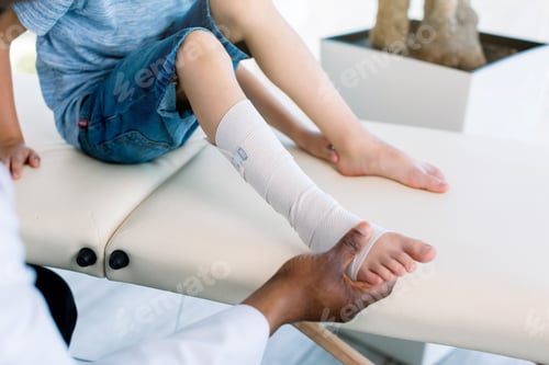 Preview: cropped shot of african american doctor putting on bandage on patients injured leg. Doctor first aid