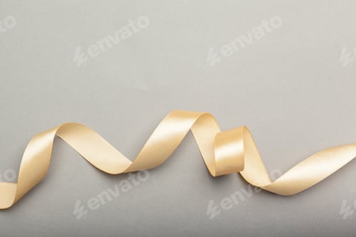 Preview: Curly gold ribbon placed on a smooth gray surface creates a simple design