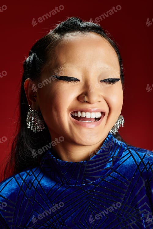 Preview: A radiant Asian woman smiles joyfully against a bold red backdrop, showcasing her elegant style