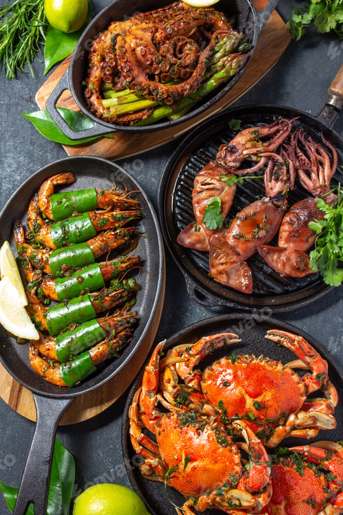 Preview: Set table with seafood dishes - cooked crabs, tiger shrimps, grilled octopus and squids on cast iron