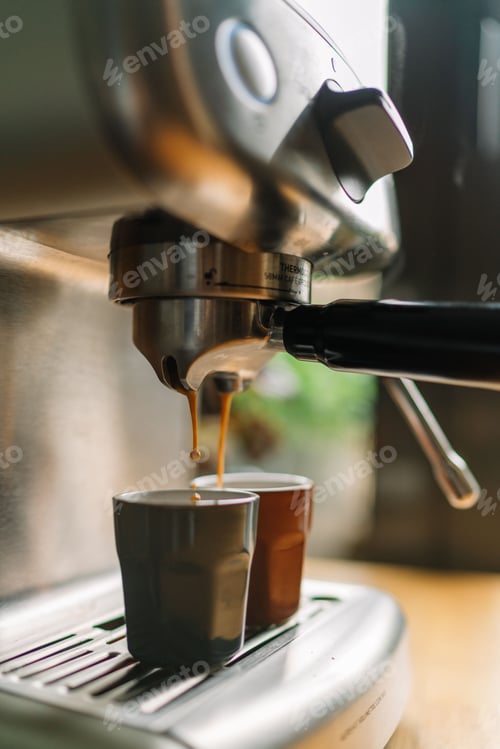 Preview: Close-up of espresso machine brewing two cups of coffee in a cozy kitchen setting.