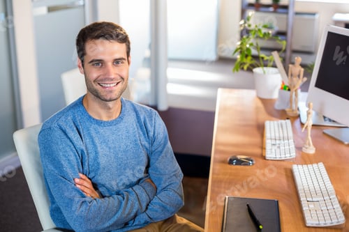 Preview: Male office worker smiling at camera sitting at office desk with keyboards and mouse, copy space