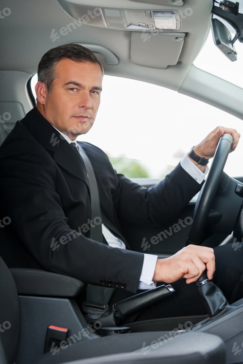 Preview: Businessman in car. Side view of confident mature businessman driving car and looking at you