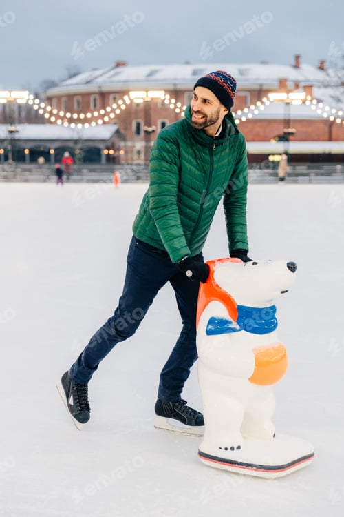 Preview: handsome bearded male being on ice rink, learns to skate with aid or prepares for skating competitio