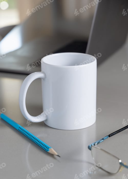 Preview: White coffee mug on grey office table against laptop, glasses and pencil closeup, mockup